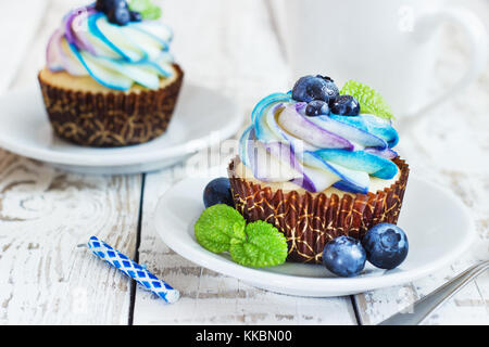 Cupcakes vanille délicate avec de la crème et des petits fruits les bleuets sur un fond de bois blanc. Banque D'Images