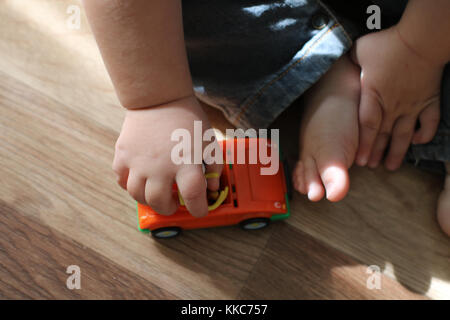 Cute little baby Playing with toy voiture sur le sol. Close up baby hands holding toy voiture et peu de pieds-nus. Banque D'Images