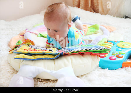 Mignon petit bébé avec les yeux bleus et cheveux gingembre lire un livre sur le lit. Banque D'Images