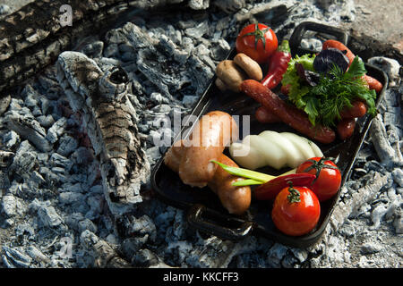 Saucisses fumées et les tomates se trouvent sur le charbon de bois. Le plat est cuit et fumé sur un charbon Banque D'Images