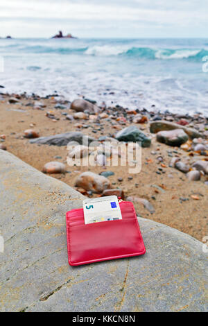 Le Trésor perdu sur le bord de la mer. La plage de galets, un petit sac à main rouge avec la remarque de cinq euros Banque D'Images