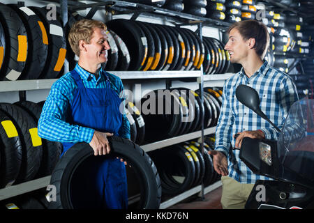 Mécanicien professionnel professionnels travaillant avec les pneus moto et en tenant au client dans shop Banque D'Images