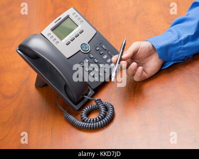 Human hand holding stylo à bille avec un téléphone sur un bureau en bois Banque D'Images