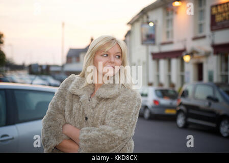 Très jolie jeune femme portant une veste style fourrure à l'extérieur dans la rue au coucher du soleil Banque D'Images