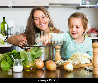 Jeune femme souriante avec petite fille cuisson de la soupe à la maison. se concentrer sur femme Banque D'Images