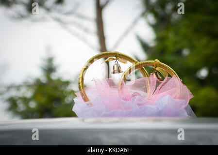 Les anneaux de mariage et de décoration sur le toit de la voiture à l'extérieur sur fond vert floue. Banque D'Images