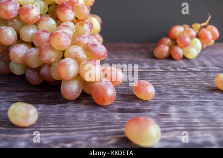 Close-up tassel de ripe green-raisins rouges et quelques baies sont situées sur la table en bois sombre. Banque D'Images