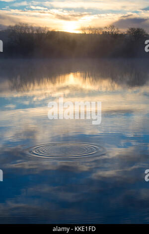 Lever du soleil et de l'eau réflexions ondulation sur un lac dans le village de Bourton on the Water. Cotswolds, Gloucestershire, Angleterre Banque D'Images