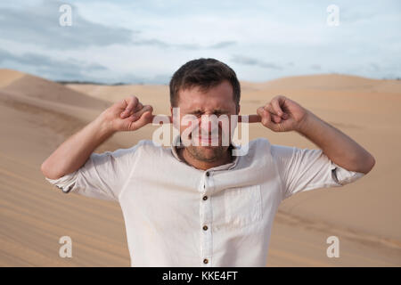 Un homme d'âge moyen est seul dans le désert et se ferme ses oreilles avec ses mains. Banque D'Images