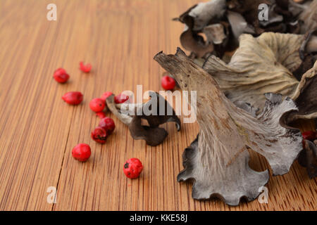 Une corne d'abondance ou Craterellus cornucopioides sur planche en bois de champignons en premier plan avec le poivron rouge et les champignons secs en arrière-plan Banque D'Images