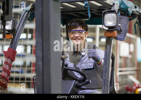 Jeune ouvrier chinois roulant chariot élévateur à l'usine Banque D'Images