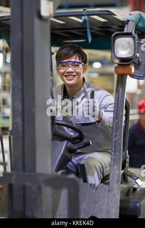 Jeune ouvrier chinois roulant chariot élévateur à l'usine Banque D'Images