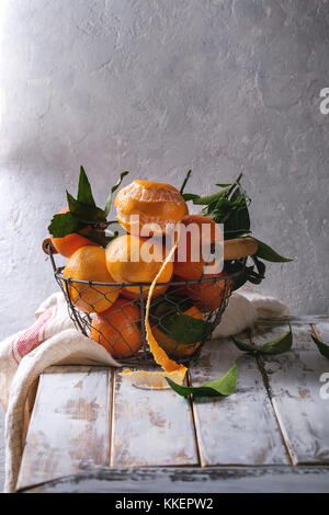 Clémentines ou mandarines biologiques mûrs avec des feuilles dans panier debout avec cuisine serviettes sur la planche en bois blanc table avec mur gris en arrière-plan. rus Banque D'Images