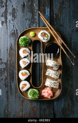 Des rouleaux de sushi set avec le saumon, les graines de sésame et d'avocat qui servent dans la plaque de bois de rose gingembre mariné, sauce soja, wasabi, côtelettes, salade d'algues Banque D'Images