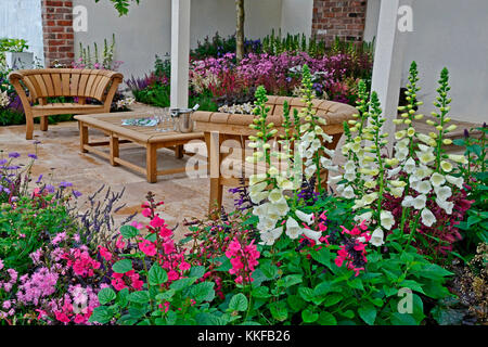 Un jardin contemporain avec terrasse et un élégant mobilier en bois entouré de fleurs colorées frontières Banque D'Images