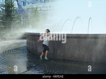 La fillette de sept ans est runing dans une éclaboussure d'eau de la fontaine. Banque D'Images