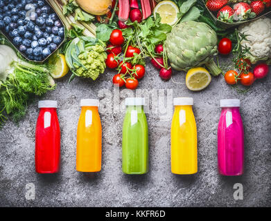 Une rouge, orange, vert, jaune et rose smoothies et jus dans des bouteilles sur fond de béton gris avec des légumes biologiques frais et fruits , être Banque D'Images