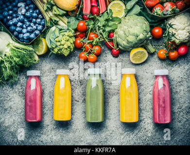 Variété de smoothies colorés ou des bouteilles de boissons alcoolisées jus avec divers ingrédients frais : fruits, baies et légumes sur bac de béton gris Banque D'Images