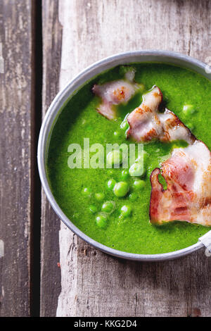 Soupe crème de pois verts en plaque en aluminium avec lard grillé. plus vieille table en bois. vue d'en haut. style rustique. Banque D'Images