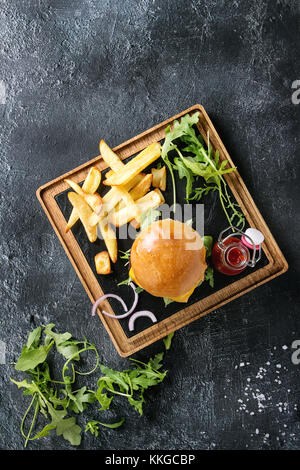 Hamburger maison traditionnelle avec du boeuf, tomate, fromage, roquette, servi sur ardoise en bois servant de sélection avec frites et sauce ketchup sur te foncé Banque D'Images