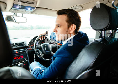 Belle beau homme élégant dans un costume d'affaires au volant d'une voiture coûteuse Banque D'Images