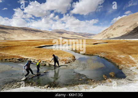 Trois personnes d'aider les uns les autres traversant un ruisseau près des sources, geyser, de Puga, le Ladakh, le Jammu-et-Cachemire, en Inde. Banque D'Images
