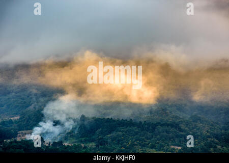 La fumée de l'incendie allumé par des nuages et des rayons de lumière dorée au coucher du soleil sur le côté du volcan agua, guatemala Banque D'Images