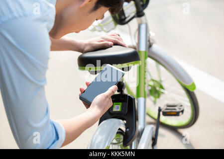 Les jeunes Chinois de la numérisation d'un QR code pour débloquer un vélo partager Banque D'Images