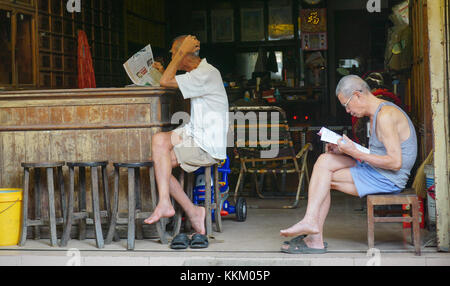 Hoi An - apirl 18, 2015. personnes âgées hommes chinois lecture journal devant sa boutique, Hoi an, Vietnam. Banque D'Images