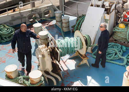 Les travailleurs sur un canal de Gozo Ferry de ligne de l'utilisation de machines et l'enroulement de la corde autour d'une étrave à mesure que le navire quitte le port. Banque D'Images