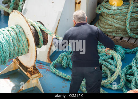 Les travailleurs sur un canal de Gozo Ferry de ligne de l'utilisation de machines et l'enroulement de la corde autour d'une étrave à mesure que le navire quitte le port. Banque D'Images