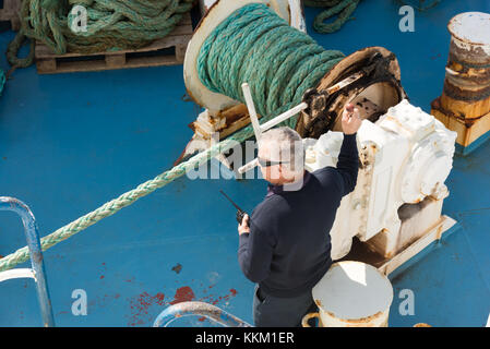 Les travailleurs sur un canal de Gozo Ferry de ligne de l'utilisation de machines et l'enroulement de la corde autour d'une étrave à mesure que le navire quitte le port. Banque D'Images