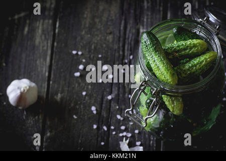 Avec bol en verre à faible teneur en sel frais concombres. sur table en bois noir avec saupoudré de sel de mer et l'ail. Meubles de style rustique, la lumière naturelle du jour. Banque D'Images