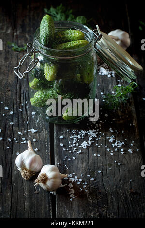 Avec bol en verre à faible teneur en sel frais concombres. sur table en bois noir avec saupoudré de sel de mer et l'ail. Meubles de style rustique, la lumière naturelle du jour. Banque D'Images