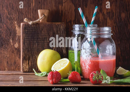 Les bocaux en verre avec smoothie vert et rouge, servi avec des épinards, citron, fraise et pomme verte sur table en bois Banque D'Images