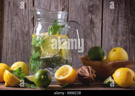 Pichet en verre de limonade fait maison, servi avec son ensemble et les tranches de citrons, limes et de menthe sur table en bois avec fond de bois. Banque D'Images