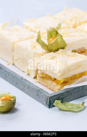 Des tranches de gâteau avec des fruits tropicaux et mousse crémeuse et mangue physalis servi en plateau en bois sur fond bleu clair Banque D'Images