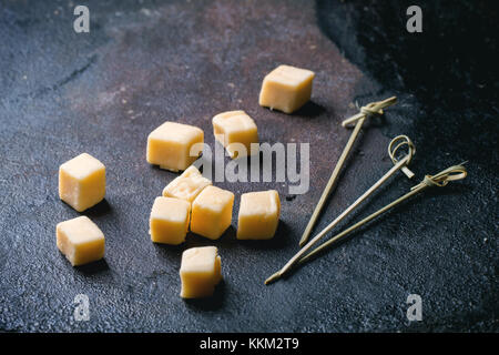 Petits cubes de fromage belge avec des bâtons à cocktail sur fond noir. vue d'en haut. Banque D'Images