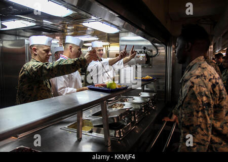 Le Capitaine de vaisseau américain Todd Vandergrift, capitaine de la station de transport amphibie USS New York (LPD 21), sert à l'alimentation avec les Marines 26e Marine Expeditionary Unit (MEU) lors d'un dîner de Thanksgiving dans l'océan Atlantique, le 23 novembre 2017. L'Iwo Jima Groupe amphibie et 26e MEU équipe a célébré Thanksgiving en mer au cours de l'exercice de l'unité de formation composite combinée. (U.S. Marine Corps photo par le Cpl. Juan A. Soto-Delgado) Banque D'Images