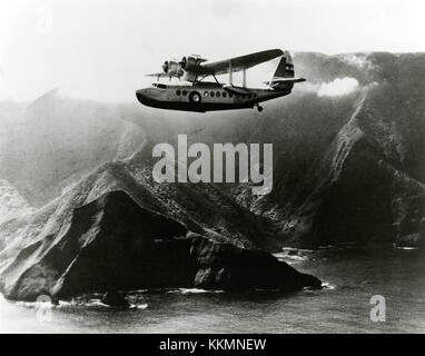 Vue du quart avant gauche de l'Inter-Island Airways Sikorsky S-43 en vol au-delà d'une côte montagneuse non identifiée quelque part dans les îles hawaïennes; vers 1935-1940. Inter-Islands Airways Sikorsky S-43 à Molokai Banque D'Images