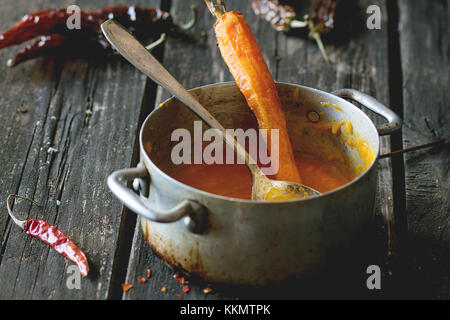 Carter d'aluminium avec des restes de soupe crème de carottes cuites au four avec de la carotte et red hot chili pepper. plus vieille table en bois avec une cuillère et pepp sec vintage Banque D'Images