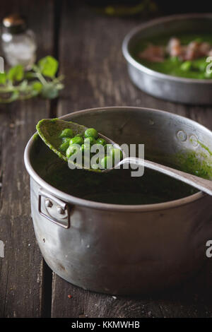 Soupe crème de petits pois dans la poêle avec une cuillère en aluminium vintage remplir les pois entiers. plus vieille table en bois sombre de style rustique., la lumière naturelle du jour. Banque D'Images