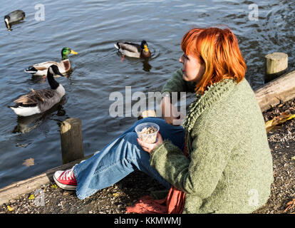 Belle fille dans sa tête rouge chez les canards du parc à l'automne Banque D'Images