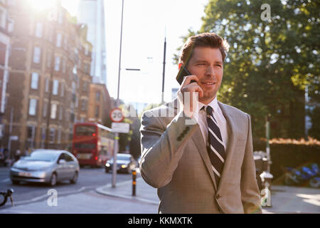 Businessman Talking On Mobile Phone à marcher le long de la rue de la ville Banque D'Images