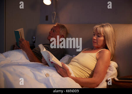 Senior Couple Wearing Pajamas Lying in Bed Reading Banque D'Images