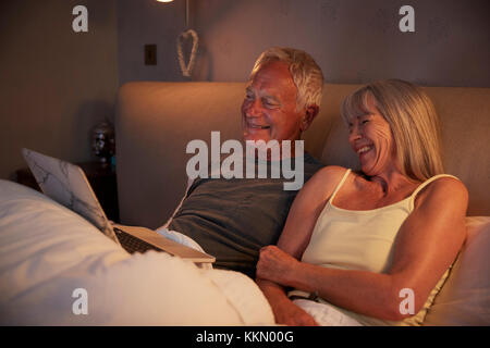 Senior Couple Wearing Pajamas Lying in Bed Looking At Laptop Banque D'Images