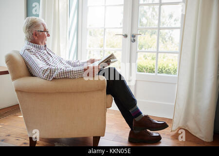 Hauts homme assis dans un fauteuil lisant le journal à la maison Banque D'Images