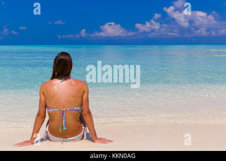 Jeune femme assise sur la rive aux Maldives. Banque D'Images