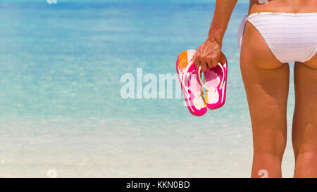 Woman holding tongs en étant debout sur la plage. Banque D'Images