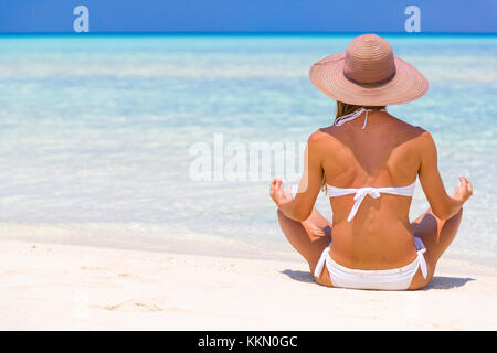 Jeune femme assise sur la rive aux Maldives avec chapeau de paille à méditer. Banque D'Images